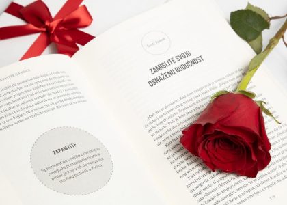 An open book with a red rose and a tied gift box next to it, conveying romance or celebration.