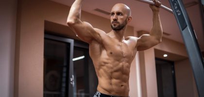 A bald, muscular man performing exercise on gym equipment indoors.