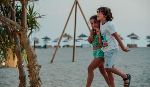 Two children enjoy a playful walk on a sandy beach, capturing summer fun.